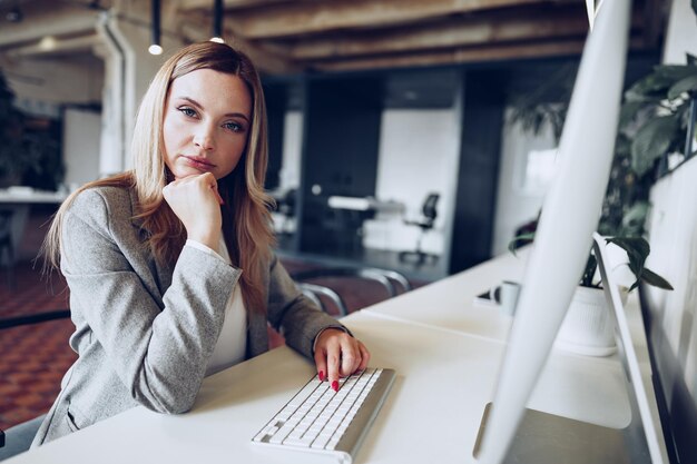 Porträt einer jungen intelligenten Geschäftsfrau, die an ihrem Arbeitstisch im Büro sitzt