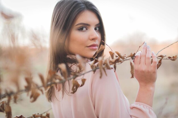 Porträt einer jungen kaukasischen Frau in einem eleganten rosafarbenen Kleid, das an einem Baum posiert