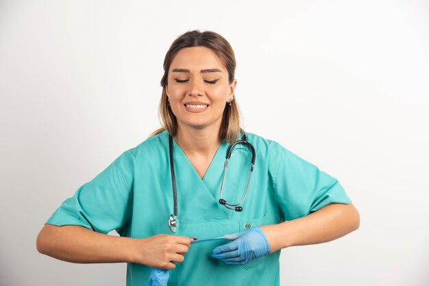 Porträt einer jungen Krankenschwester, die versucht, medizinische Latexhandschuhe auszuziehen.