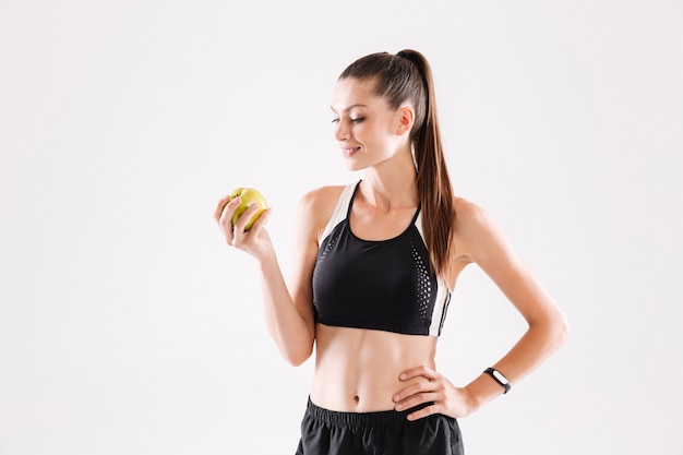 Porträt einer jungen lächelnden Sportlerin, die grünen Apfel hält