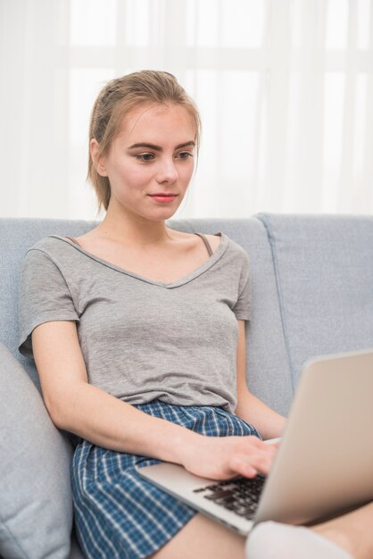 Porträt einer jungen lesbischen Frau, die auf Sofa unter Verwendung des Laptops sitzt