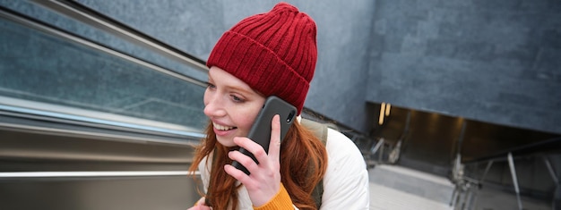 Kostenloses Foto porträt einer jungen rothaarigen frau, die durch die stadt geht und mit eingeschaltetem mobiltelefon die treppe hinaufsteigt