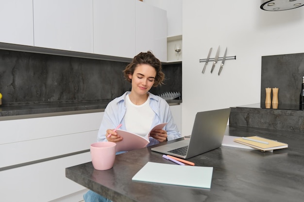 Kostenloses Foto porträt einer jungen schönen frau, die zu hause studiert, ihre arbeitsmappe umblättert, arbeiten von zu hause aus mit dem laptop umblättert