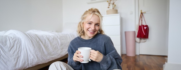 Kostenloses Foto porträt einer jungen schönen frau in lässiger kleidung, die mit einer tasse tee auf dem schlafzimmerboden sitzt