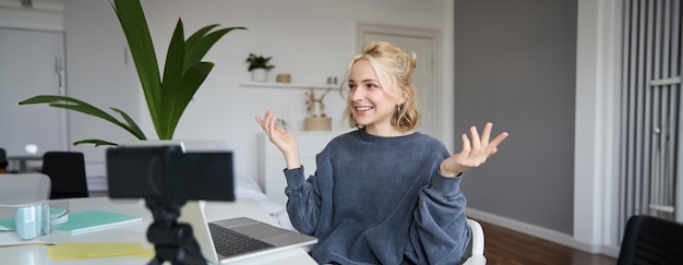 Porträt einer jungen Social-Media-Content-Schöpferin sitzt in einem Raum mit Laptop und digitaler Kamera