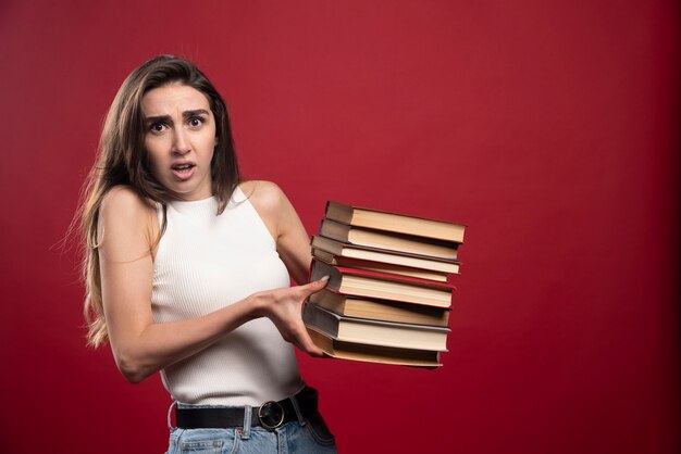 Porträt einer jungen Studentin, die viele Bücher trägt