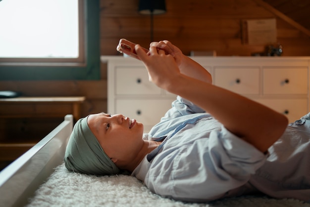 Kostenloses Foto porträt einer krebskranken frau, die ihr smartphone zu hause benutzt