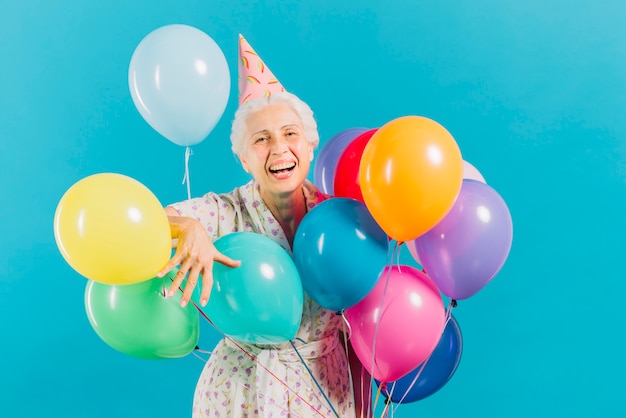 Porträt einer lächelnden älteren Frau mit bunten Ballonen auf blauem Hintergrund