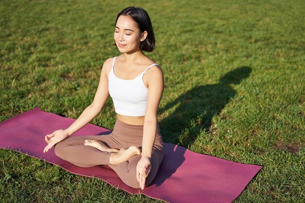 Porträt einer lächelnden asiatischen Frau, die beim Yoga an der frischen Luft meditiert und sich auf Gummimatten entspannt