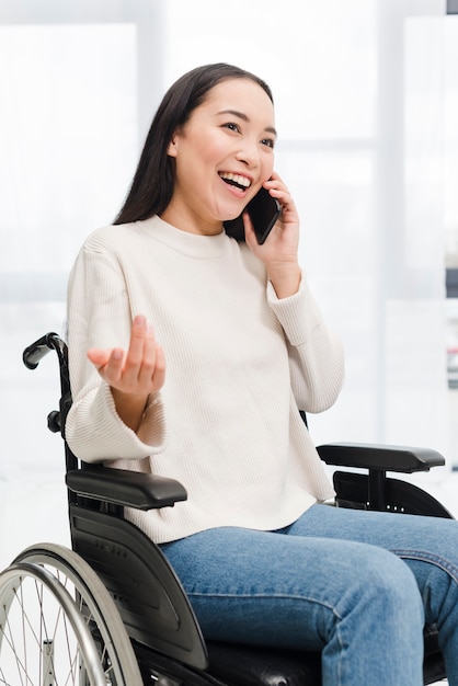 Porträt einer lächelnden behinderten jungen Frau, die auf dem Rollstuhl sitzt, zuckend mit dem Handy