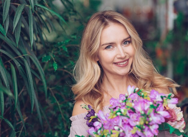 Porträt einer lächelnden blonden jungen Frau, die Blumenblumenstrauß hält