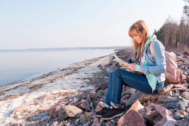 Porträt einer lächelnden jungen Frau, die auf dem Strand betrachtet Karte sitzt
