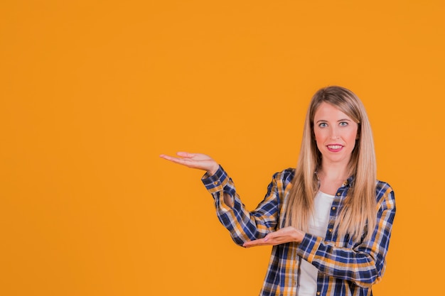 Porträt einer lächelnden jungen Frau, die etwas gegen einen orange Hintergrund darstellt