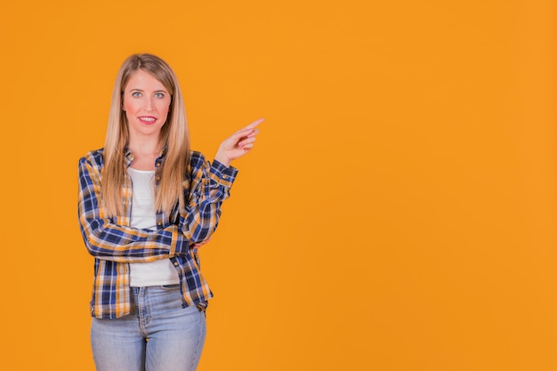 Porträt einer lächelnden jungen Frau, die ihren Finger gegen einen orange Hintergrund zeigt