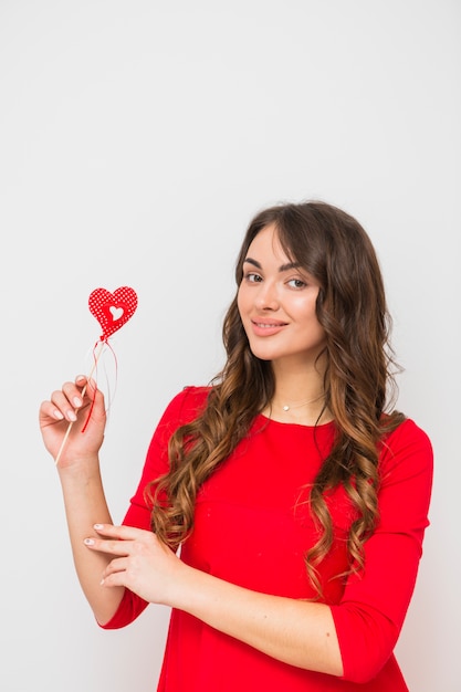 Porträt einer lächelnden jungen Frau, die in der Hand rote Herzform lokalisiert auf weißem Hintergrund hält