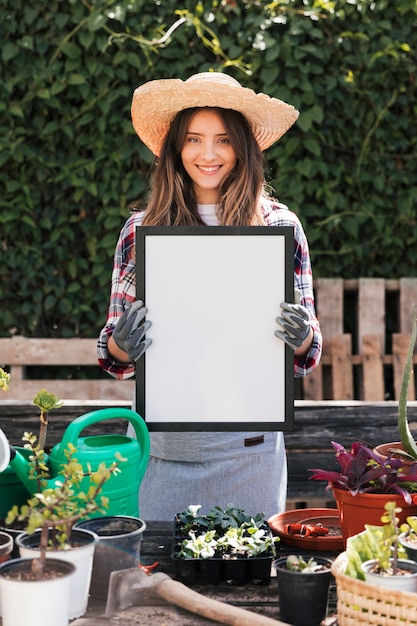 Porträt einer lächelnden jungen Frau, die in der Hand weißen leeren Rahmen hält