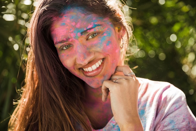 Porträt einer lächelnden jungen Frau mit rosa und blauem holi Pulver auf ihrem Gesicht im Sonnenlicht