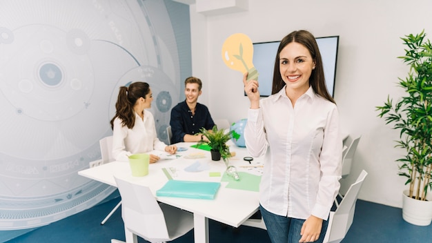 Porträt einer lächelnden jungen Geschäftsfrau mit der Glühlampeikone, die im Büro steht