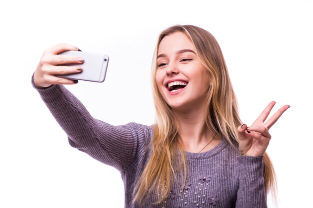 Porträt einer lächelnden niedlichen Frau, die Selfie-Foto auf Smartphone lokalisiert auf einer weißen Wand macht