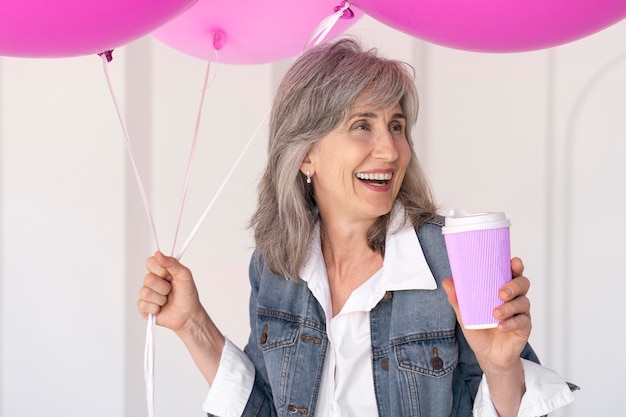 Porträt einer lächelnden Seniorin mit Tasse und rosa Luftballons