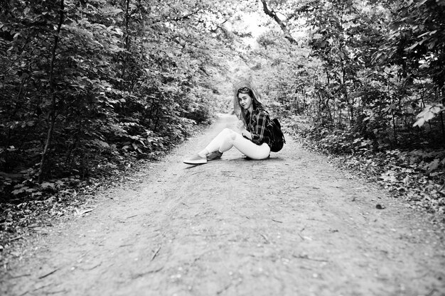 Porträt einer positiven jungen wunderschönen Blondine, die mit einer Karte in ihren Händen im Wald auf dem Boden sitzt