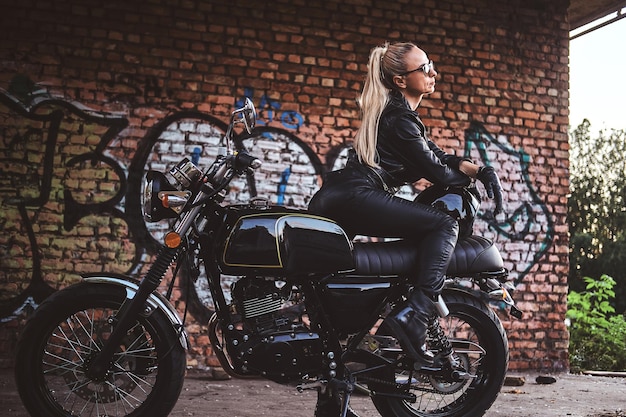 Kostenloses Foto porträt einer reifen, attraktiven dame neben ihrem oldtimer-motorrad und ihrer graffiti-ziegelwand.
