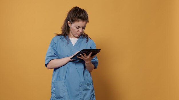 Porträt einer Ärztin, die ein Tablet hält und Patientendaten in Krankenhausuniform im Studio eingibt. Professioneller Sanitäter mit moderner digitaler Touchscreen-Technologie für das Gesundheitskonzept.