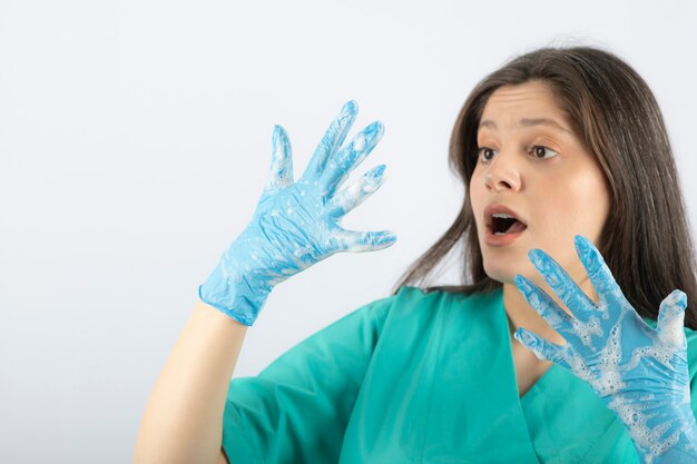 Porträt einer schockierten Krankenschwester oder eines Arztes in grüner Uniform, die Handschuhe ansieht.