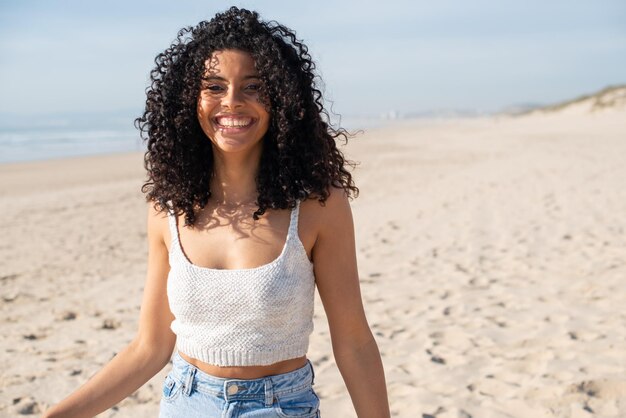 Porträt einer schönen afroamerikanischen Frau am Strand. Weibliches Model mit lockigem Haar und strahlendem Lächeln, das in die Kamera schaut. Porträt, Schönheitskonzept