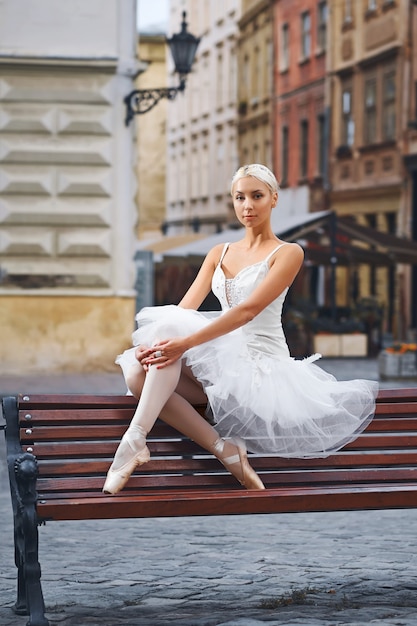 Porträt einer schönen Balletttänzerin, die auf der Bank im Stadtzentrum ruht und anmutig städtisches Modekonzept der Schönheitseleganz sitzt.