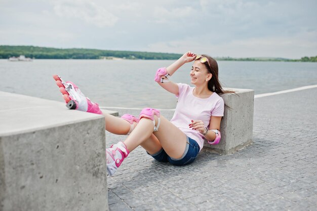 Porträt einer schönen Frau, die auf dem Boden neben einem Betonwürfel sitzt und Rollerblades und Freizeitkleidung trägt