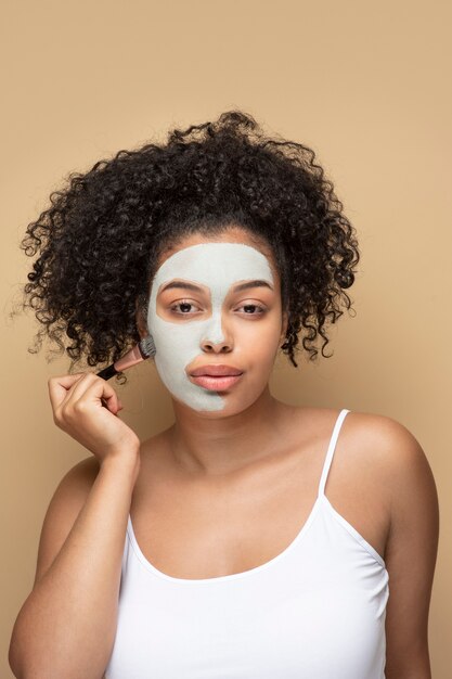 Porträt einer schönen Frau, die Gesichtsmaske mit einem Make-up-Pinsel auf ihrem Gesicht aufträgt