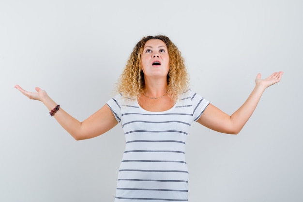 Kostenloses Foto porträt einer schönen frau, die handflächen beiseite ausbreitet, während sie im t-shirt nach oben schaut und erstaunte vorderansicht schaut