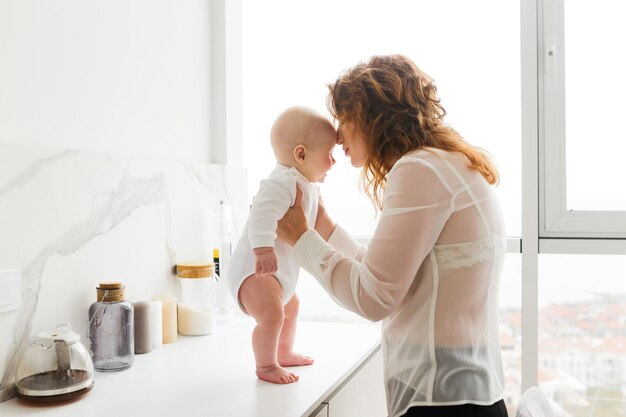 Porträt einer schönen Frau, die steht und ihr hübsches kleines Baby in den Händen hält