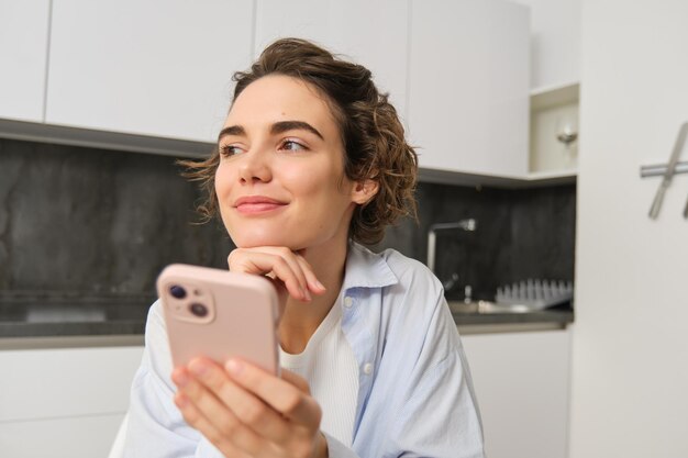 Porträt einer schönen Frau zu Hause, die ein Smartphone in der Hand hat und von einer Handy-App aus online einkaufen geht