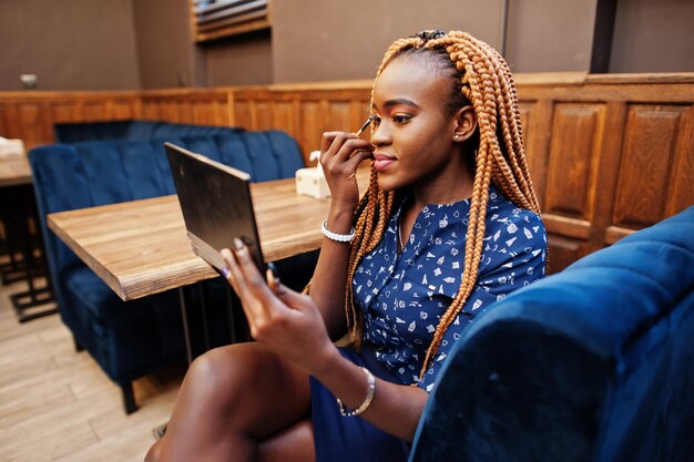 Porträt einer schönen jungen afrikanischen Geschäftsfrau mit blauer Bluse und Rock, die Make-up-Palette hält und sich vorbereitet