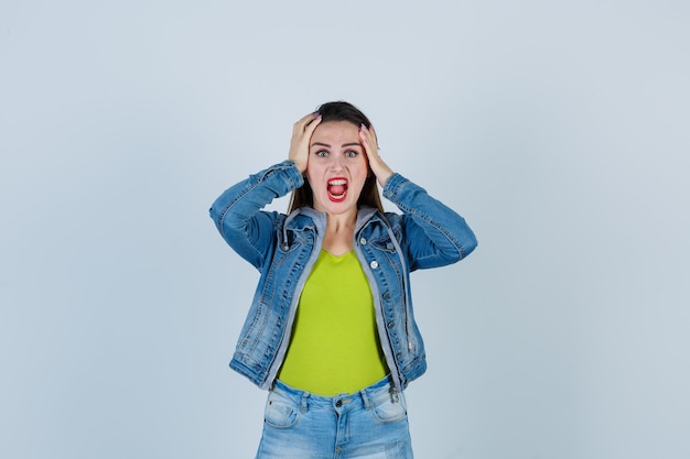 Porträt einer schönen jungen Dame, die in Denim-Outfit die Hände auf dem Kopf hält und aggressive Vorderansicht sieht