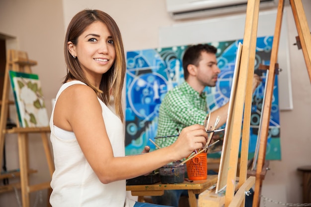 Porträt einer schönen jungen Frau, die an einem Gemälde in einer Kunstschule arbeitet