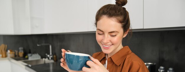 Kostenloses Foto porträt einer schönen jungen frau, die das köstliche aroma von frisch gebackenem kaffee mit einem becher genießt