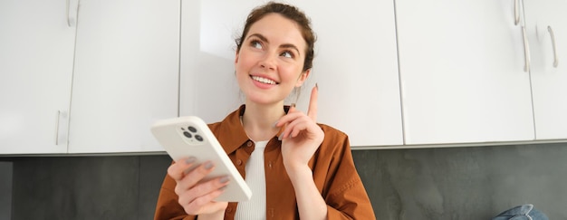 Porträt einer schönen jungen Frau, die mit einem zufriedenen Gesicht lächelt und über eine Smartphone-Anwendung nachdenkt