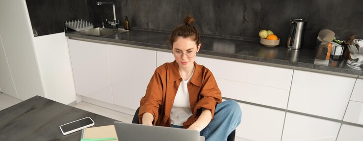 Kostenlose Foto porträt einer schönen jungen frau, die zu hause studiert und mit laptop und dokumenten in der küche sitzt
