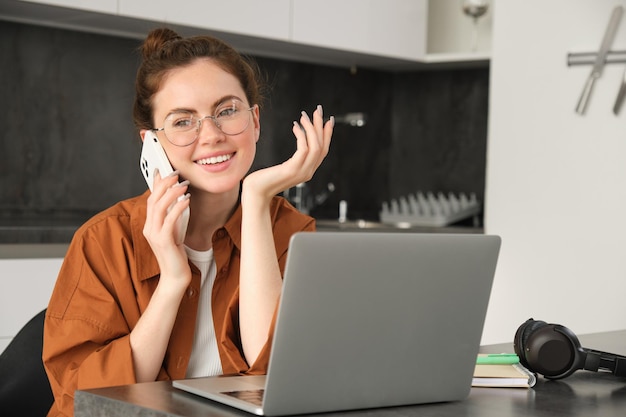 Kostenloses Foto porträt einer schönen lächelnden frau, die von zu hause aus arbeitet und über ein handy spricht, das einen kunden anruft