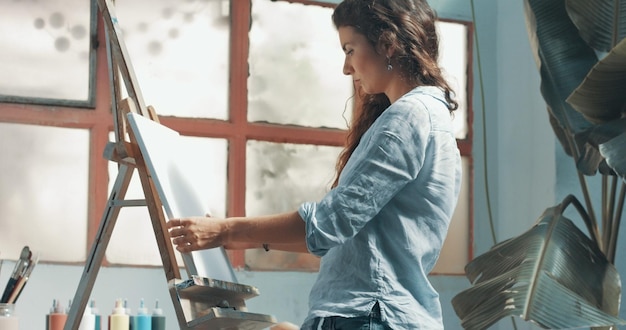 Porträt einer schönen langhaarigen Künstlerin bei der Arbeit an ihrer Leinwand in einem Studio