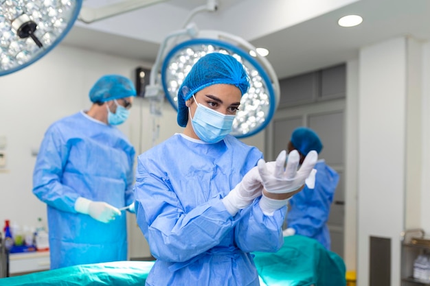 Porträt einer schönen Ärztin, die medizinische Handschuhe anzieht, die im Operationssaal stehen Chirurg im modernen Operationssaal