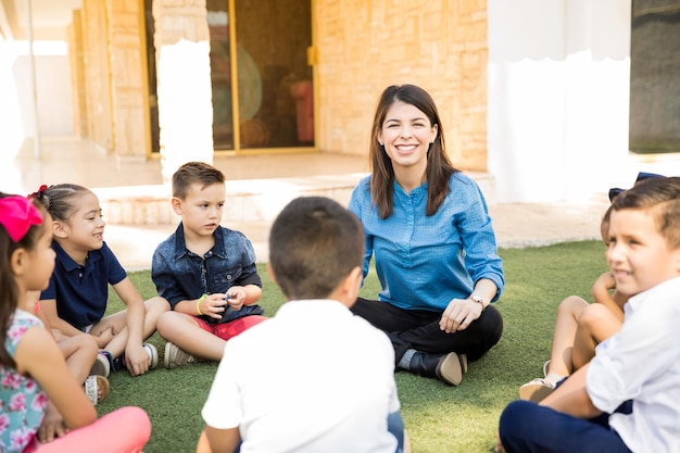 Porträt einer schönen Vorschullehrerin, die mit einer Gruppe von Schülern im Freien eine Klasse hat und lächelt