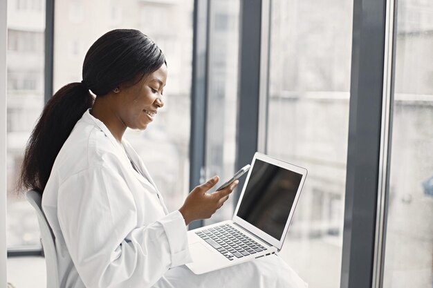 Porträt einer schwarzen Ärztin, die in ihrem Büro in der Klinik sitzt und einen Laptop benutzt