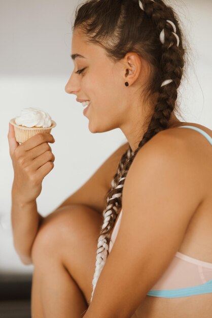 Porträt einer sexy jungen Frau, die Cupcake auf einer weißen Wand isst