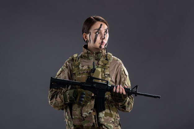 Porträt einer Soldatin in Tarnung mit Maschinengewehr an der dunklen Wand