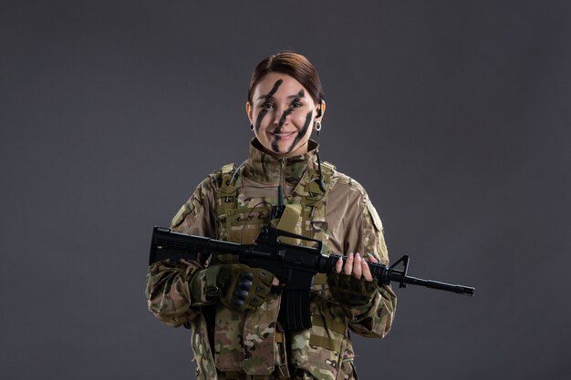 Porträt einer Soldatin in Tarnung mit Maschinengewehr an der dunklen Wand