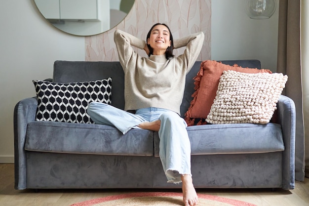 Porträt einer sorglosen asiatischen Frau, die den freien Tag genießt, auf dem Sofa sitzt und lächelt, freut sich, sich in hou zu entspannen
